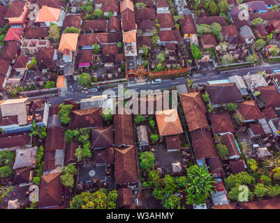 Viele Villen mit braun-orange Schindeldächer zwischen tropischen Bäumen am Himmel Hintergrund in Ubud auf Bali. Sonne scheint auf Sie. Antenne horizontal Stockfoto