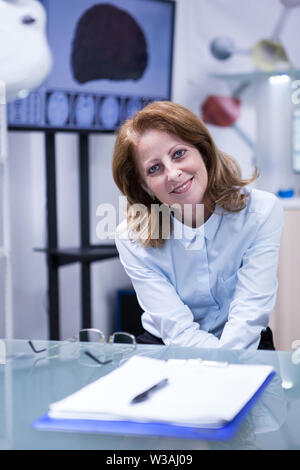 Mittleres Alter Dame lächelnd in die Kamera nach unten sitzen in einem modernen Labor. Mittleres Alter Arzt im Krankenhaus Labor. Stockfoto