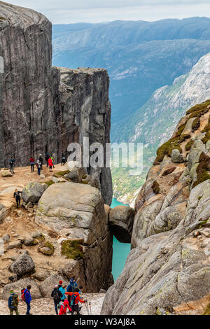 Kjeragbolten, Blick von oben auf den Stein, eingeklemmt zwischen zwei Felsen mit Fjord im Hintergrund und Touristen versammelt, Lysefjord, Norwegen Stockfoto