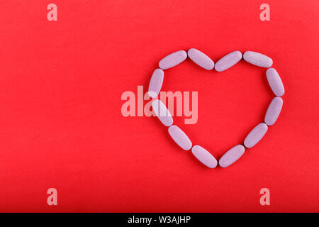 Oval rosa Pillen, die in der Form eines Herzens auf einem hellen roten Hintergrund. Platz für Text Stockfoto