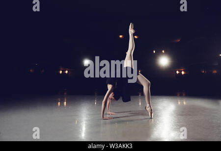 Ballerina in einen schwarzen Anzug ist das Springen auf einem schwarzen Hintergrund in Szene. Stockfoto