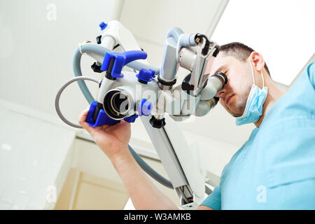 Männliche Zahnarzt suchen durch ein Mikroskop in einer Zahnarztpraxis. Stockfoto