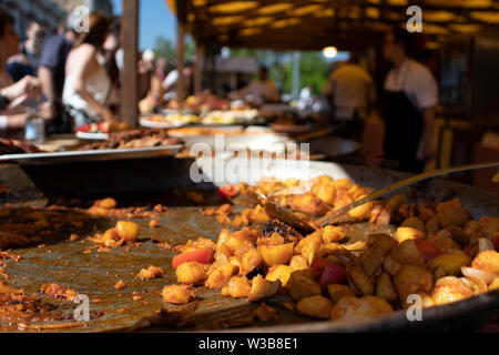 Street Food Festival in Budapest, Ungarn. Ein riesiger Topf mit traditionellen lokalen Hühnereintopf, halb leer. Man bedient Kunden im Hintergrund. Stockfoto