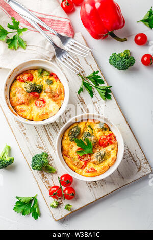 Frittata mit Brokkoli in zwei keramischen Formen. Frittata mit Brokkoli, süßer Paprika und Tomaten in zwei keramischen Formen zum Backen. Italienische Omelette w Stockfoto