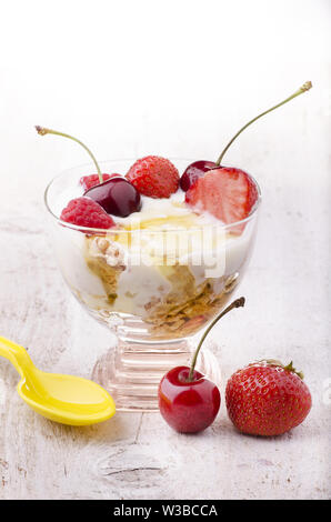 Exquisite Tasse mit frischem Joghurt, Honig und Obst mit Kirschen, Erdbeeren und Himbeeren Stockfoto