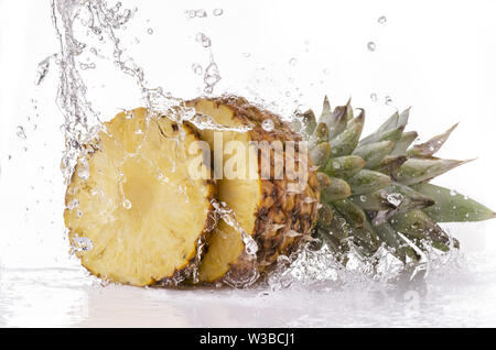 Eine Welle von klarem Wasser fällt auf Reife und geschnittene Ananas auf weißem Hintergrund Stockfoto