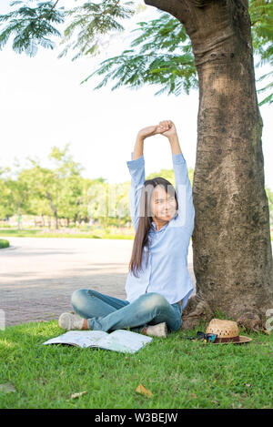 Entspannt junge schöne Frau ein Blaues T-Shirt mit lächelnden Gesicht im Park tragen. Zeit zum Entspannen nach der Arbeit. Horizontale. verschwommenen Hintergrund. Film Effekt. Stockfoto