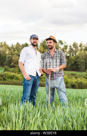 Zwei Mann in Plaid Shirt im oat Feld mit Wald im Hintergrund und Sprechen Stockfoto