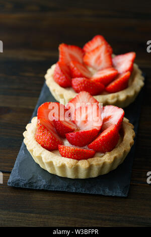 Törtchen mit Vanillesauce und frische Erdbeeren auf einer Schiefertafel Platte serviert. Dunkler Holztisch, hohe Auflösung Stockfoto