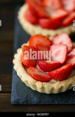 Törtchen mit Vanillesauce und frische Erdbeeren auf einer Schiefertafel Platte serviert. Dunkler Holztisch, hohe Auflösung Stockfoto