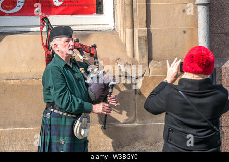 Mann für ein Foto posieren, Dudelsack spielen im traditionellen Kilt, außerhalb der Straßenmusik im Sonnenschein auf der Royal Mile in Edinburgh, Schottland, Großbritannien. Stockfoto