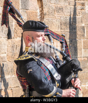 Mann spielt Dudelsack in traditioneller Kleidung, Straßenmusik, draußen im Sonnenschein auf der Royal Mile in Edinburgh, Schottland, Großbritannien. Stockfoto