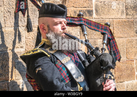 Mann spielt Dudelsack in traditioneller Kleidung, Straßenmusik, draußen im Sonnenschein auf der Royal Mile in Edinburgh, Schottland, Großbritannien. Stockfoto