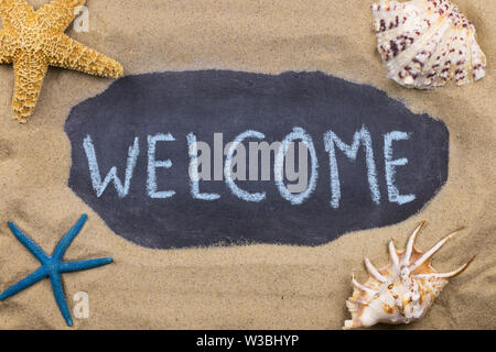 Handschriftliche chalk Inschrift Willkommen auf Tafel, unter den Muscheln und Seesterne auf dem Sand liegen. Ansicht von oben Stockfoto