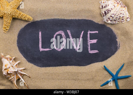 Handschriftliche chalk Inschrift Liebe auf Tafel, unter den Muscheln und Seesterne auf dem Sand liegen. Ansicht von oben Stockfoto