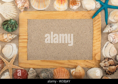Rahmen aus Holz auf dem Sand, Sterne, Muscheln und Steine um. Mit Platz für Design, Text platzieren. Ansicht von oben Stockfoto