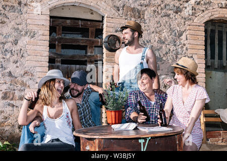 Portrait von glücklichen jungen Menschen zusammen sitzen und Lachen, während sie auf einer Party mit Bier auf den Tisch. Stockfoto