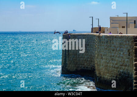 Akko, Israel - 08 Juli, 2019: Junge arabische Menschen springen von der Mauer zum Meer, mit anderen beobachten, in der Altstadt von Akko (Akko), Israel Stockfoto