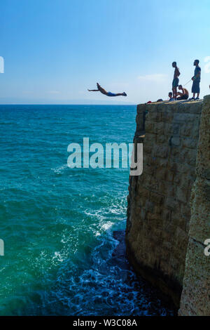 Akko, Israel - 08 Juli, 2019: Junge arabische Menschen springen von der Mauer zum Meer, mit anderen beobachten, in der Altstadt von Akko (Akko), Israel Stockfoto