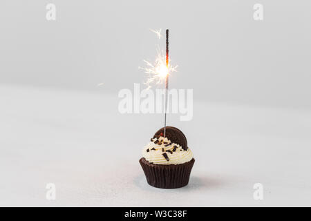 Essen, Party und Urlaub Konzept - Geburtstag Cupcake mit Wunderkerzen auf weißem Hintergrund Stockfoto