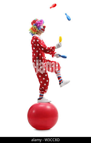 Volle Länge geschossen von einem Clown jonglieren und stehen auf einer Kugel auf weißem Hintergrund Stockfoto