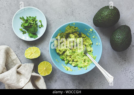 Pürierte avocado guacamole Sauce in blau Keramik Schüssel auf grauem Beton Hintergrund. Tabelle Ansicht von oben. Gesund vegan vegetarische Kost, Brotaufstrich oder zu Stockfoto