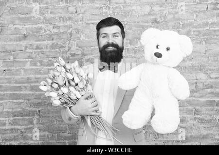 Macho fertig, romantisches Date. Warten auf Darling. Mann gut gepflegt Verschleiß tuxedo Bow Tie halten Blumen Tulpen Bouquet und großen Teddybären Spielzeug. Laden Sie dating. Romantisches Geschenk. Romantischen Mann. Stockfoto