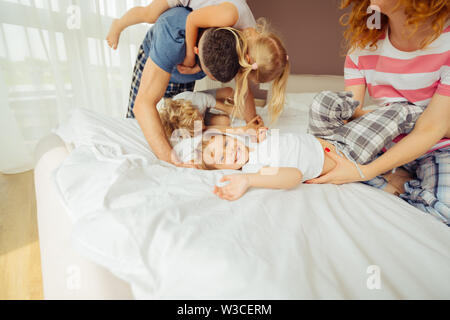 Aufrichtige Gefühle. Freut mich glücklich das Kind auf dem Bett, während Spaß mit Ihrer Familie Stockfoto