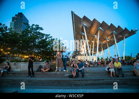 LONG ISLAND CITY, NEW YORK - Juli 13, 2019: Blick auf Gantry Plaza Park an einem Sommerabend mit Menschen sichtbar. Stockfoto