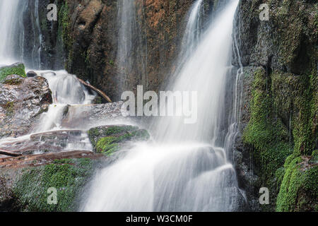 Close up Details der Wasserfall stream. schnelle Strömung mit einer langen Belichtungszeit. Feuchten moosbedeckten Felsbrocken. gefallene Laub, Zweige und Reisig. erfrischende Natur backgro Stockfoto