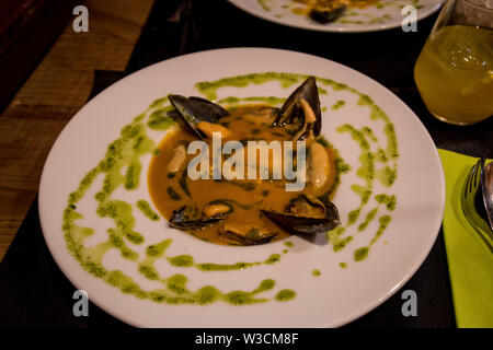 Vier Muscheln gekocht in eine Tomate mit grünen Dressing Stockfoto