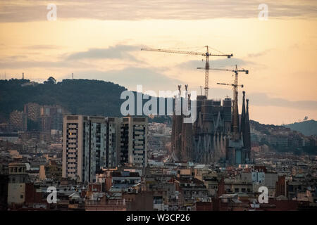 Ein Blick auf die noch im Bau der Sagrada Familia mit der Konstruktion für Krane bei Sonnenuntergang mit Bergen im Hintergrund Stockfoto