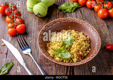 Couscous in Schüssel mit Olivenöl und getrockneten Tomaten auf Holzuntergrund, orientalische Küche, horizontale Foto, in der Nähe Stockfoto