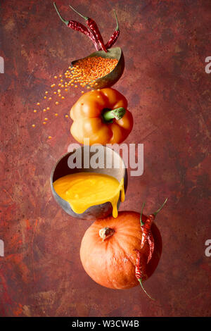 Kürbis, Pfeffer und orange Linsensuppe und seine Inhaltsstoffe, Balance und Levitation auf dunklem Hintergrund rot Stockfoto