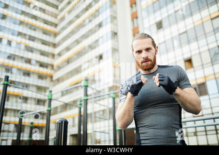 Sicher gutaussehenden jungen Mann mit dem roten Bart tragen fingerlose handschuhe Üben allein Kickboxen am Sportplatz Stockfoto