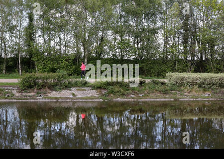 Reflexion einer Frau Jogger in rosa Top und schwarze Leggings rund um den Park See an der Victoria Road, Belfast, Nordirland. Stockfoto