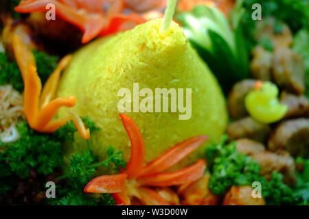 Ein traditionelles indonesisches Essen, das bei besonderen Veranstaltungen hergestellt wird. Nasi Tumpeng symbolisiert Dankbarkeit gegenüber Gott. Die gelbe Reisfarbe symbolisiert Wohlbefinden. Stockfoto