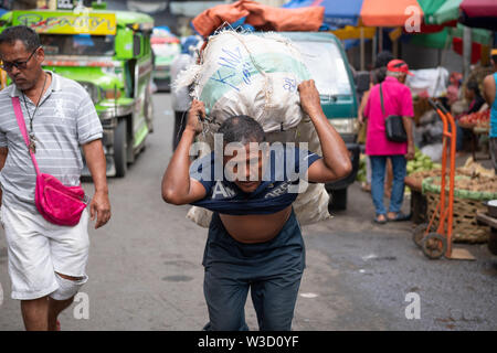 Ein Filipino Mann trägt eine schwere Last von Gemüse auf dem Markt von Cebu City, Philippinen Stockfoto