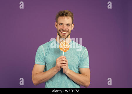 Geschmack der Kindheit. Mann mit Borsten mag Lollipop. Cheat meal Konzept. Zucker schädlich für die Gesundheit. Kerl halten Lollipop candy violett unterlegt. Mann schöner macho Essen großen bunten süßen Lutscher. Stockfoto