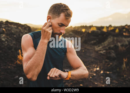 Männliche Läufer Synchronisierung Drahtloser Ohrhörer mit smart Watch. Vorbereitung für Trail Running im Freien bei Sonnenaufgang. Stockfoto