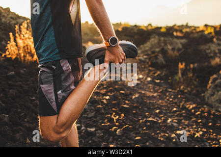 Männliche Läufer stretching Beine und Füße und die Vorbereitung für den Betrieb im Freien. Smartwatches oder Fitness Tracker auf der Hand. Schöne Sonne Licht auf Hintergrund. Ac Stockfoto