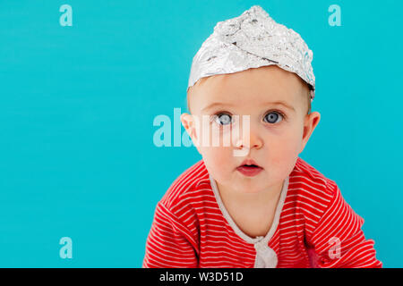 Baby in eine Folie Hut sitzt auf einem blauen Hintergrund Stockfoto