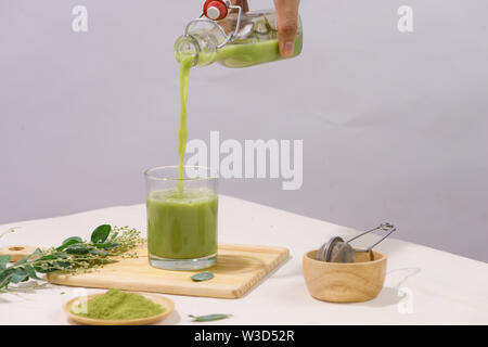 Grüner Tee wird in Glas Tee Tasse auf weißem Tabelle gegossen Stockfoto