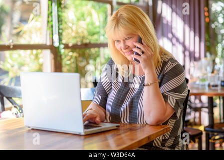 Portrait von Beschäftigte Umsatz plus size Frau im Cafe sitzen und über Ihr Smartphone. Geschäftsfrau, das online arbeitet. Attraktive reife Geschäftsfrau workin Stockfoto