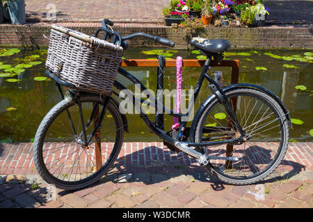 Leiden, Holland - Juli 05, 2019: Altes Fahrrad mit Korb in der Nähe der kleinen Kanal geparkt Stockfoto