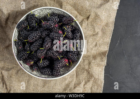 Frische rohe Maulbeeren in der Platte auf dunklen konkreten Hintergrund. Ansicht von oben mit der Kopie. Flach Hintergrund Stockfoto