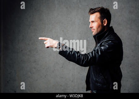 Ernster Mann in Leder Jacke zeigt. Gegen eine Betonwand Stockfoto