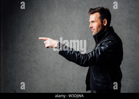 Ernster Mann in Leder Jacke zeigt. Gegen eine Betonwand Stockfoto