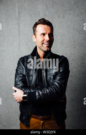 Glückliche junge Mann in der Lederjacke gegen die Betonwand stehend, weg schauen Stockfoto