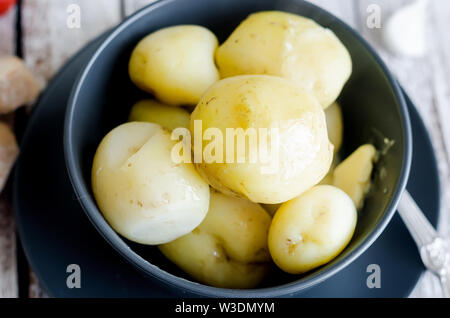 Leckere Junge gekochte Kartoffeln mit Dill, dünn und Zwiebeln in Schwarz auf Weiß Schüssel rustikalen Holztisch Stockfoto
